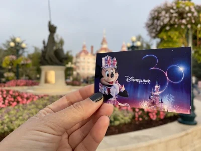 Mano de Mónica Ferreiro (El Viaje de Sofi) sujetando una entrada para Disneyland Paris frente a la entrada.