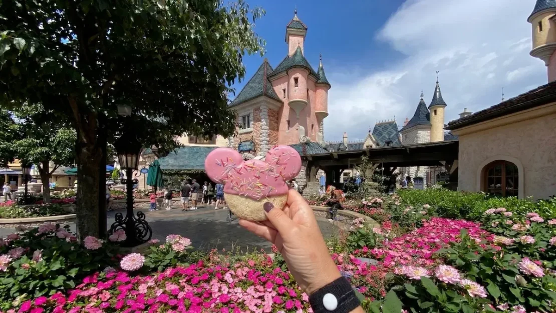 Primer plano de un donut con forma de Mickey Mouse en Fantasyland de Disneyland París con el castillo de fondo.