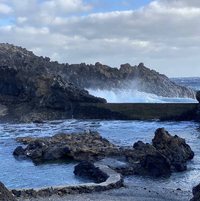 Piscina natural Charco del Palo en Lanzarote, rodeada de rocas volcánicas negras y mar azul.
