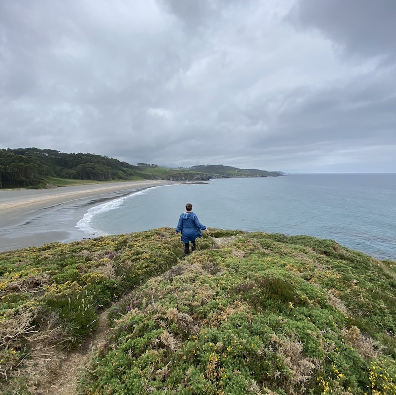 Mónica en la playa de Frejulfe, Asturias, bajo un cielo gris típico del paisaje del norte de España.