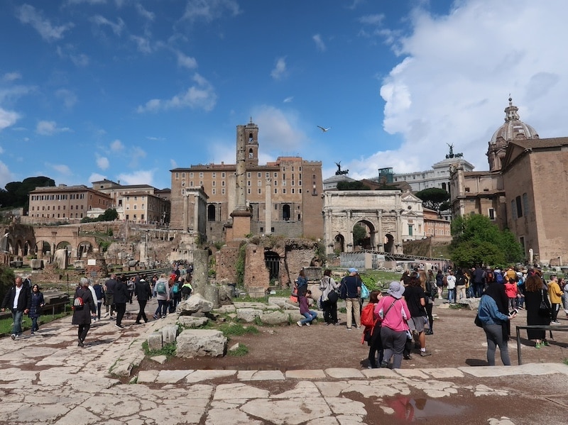 Turistas recorriendo las ruinas del Foro Romano en una visita guiada bajo el sol.
