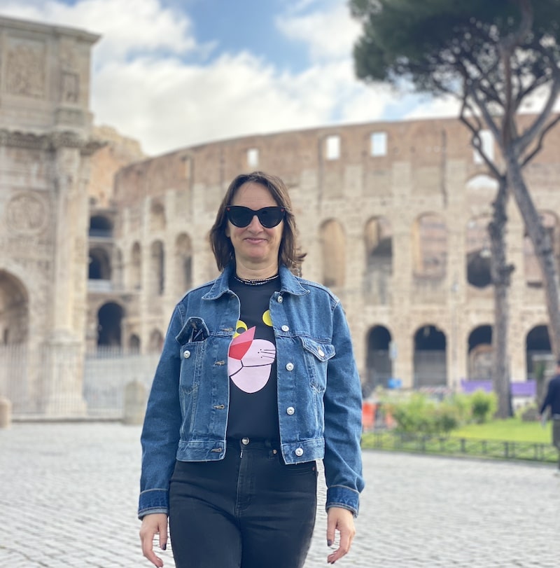 Mónica de El Viaje de Sofi sonriendo frente al Coliseo y el Arco de Tito en el Foro Romano durante su viaje a Roma.