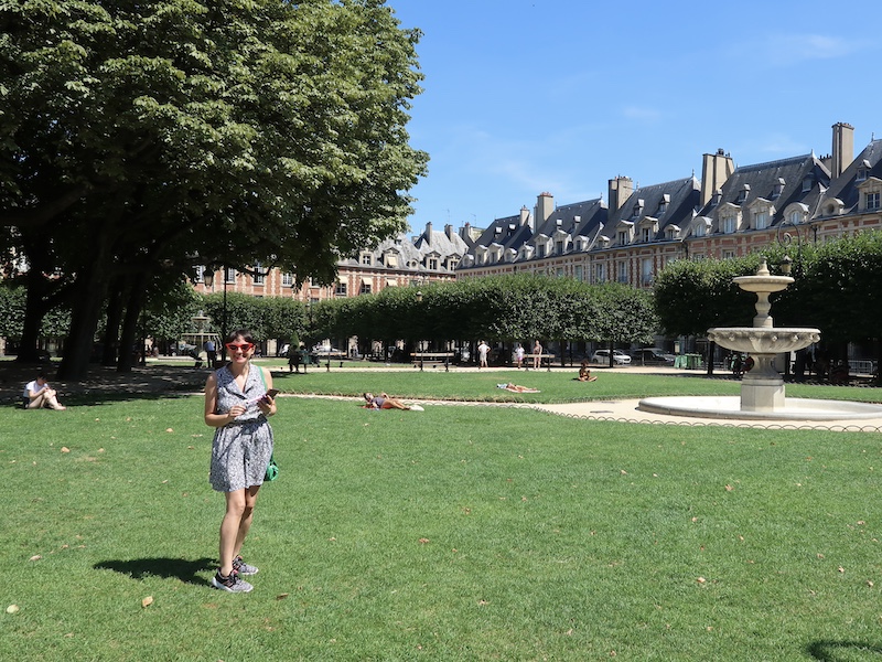 Viajera sentada sobre el césped en la Plaza de Vosgos, rodeada de arquitectura clásica