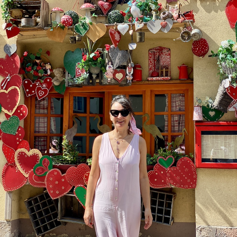 Sofi posando delante de una ventana tradicional decorada con flores en Colmar, Alsacia.