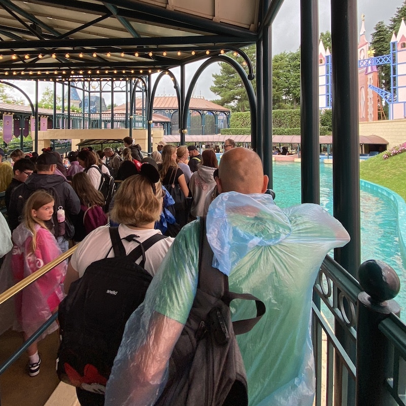 Gente con chubasqueros haciendo cola bajo la lluvia en las atracciones de Disneyland Paris.