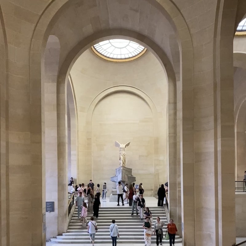 Estatua helenística de la Victoria de Samotracia sobre un pedestal en forma de proa de barco en la escalera Daru del Louvre.