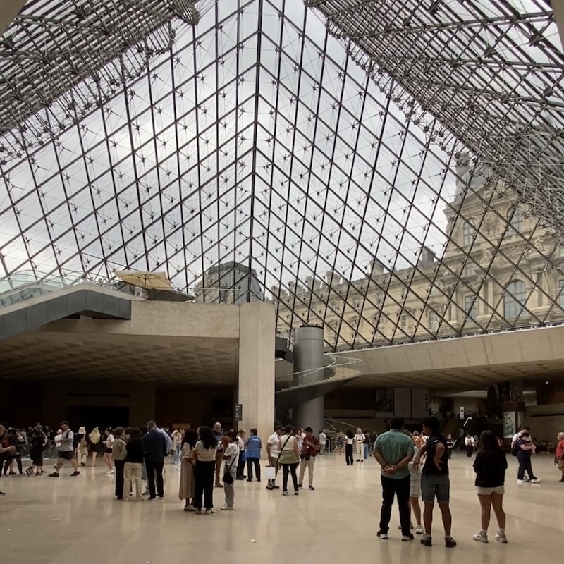 Vista interior de la pirámide de cristal del Museo del Louvre desde el Hall Napoleón con luz natural.