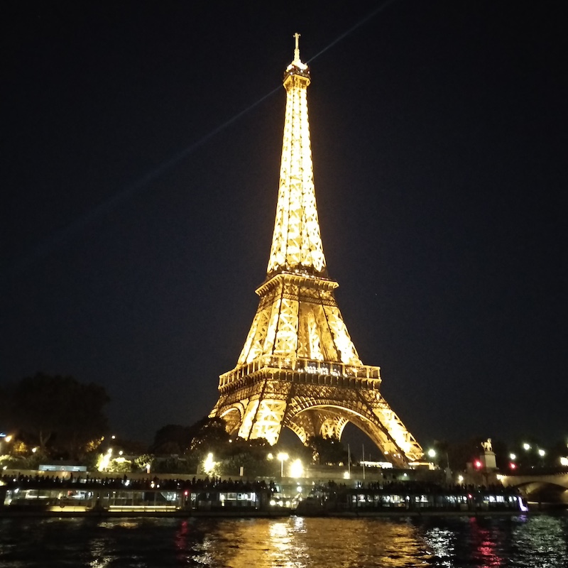 Vista nocturna de la Torre Eiffel en París, completamente iluminada en dorado con sus destellos activados sobre el cielo oscuro.