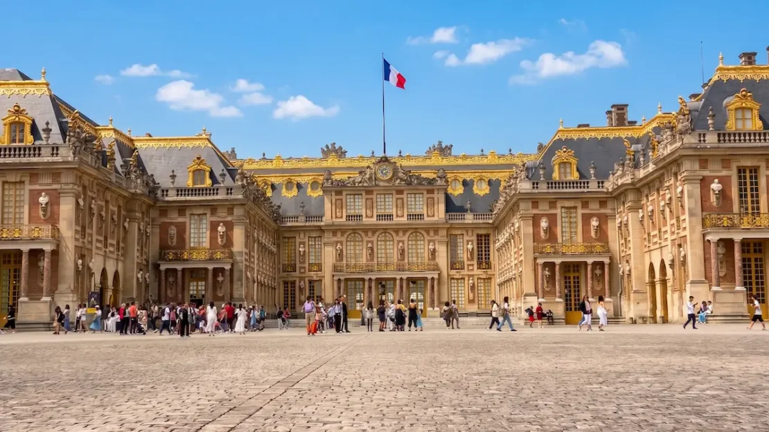 Fachada principal del Palacio de Versalles bajo un cielo azul despejado en verano.