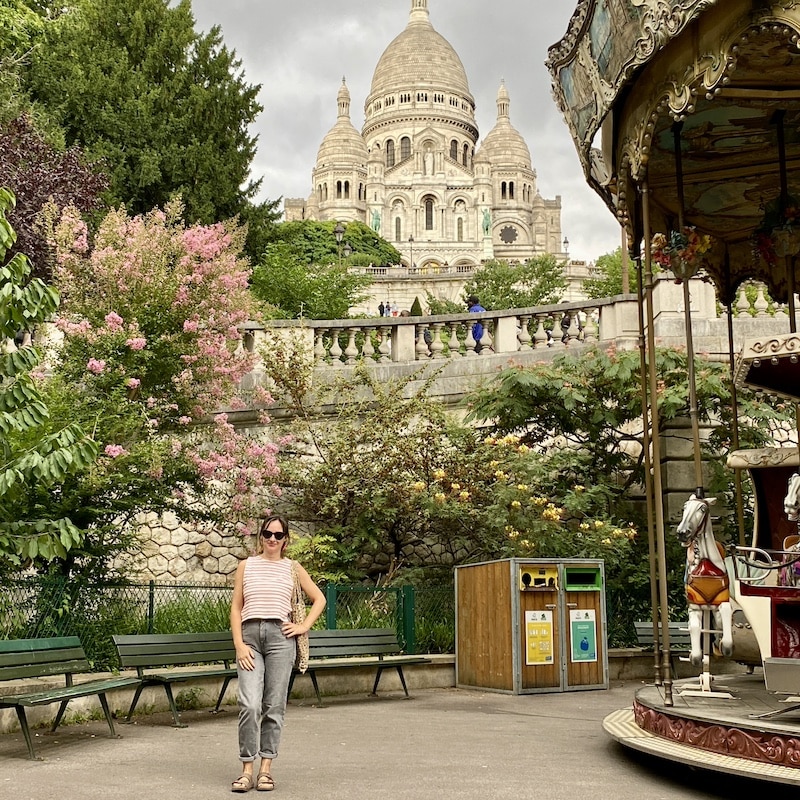 El Viaje de Sofi posando en con el tiovivo antiguo de Montmartre y la Basílica del Sagrado Corazón al fondo en París.