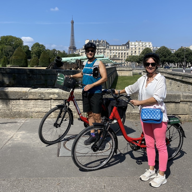 Pareja con bicis y casco frente a la Torre Eiffel durante un tour en bicicleta por Paris en español