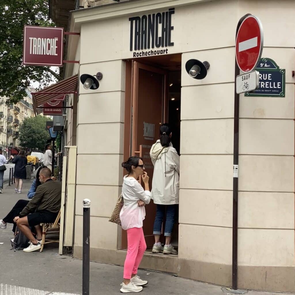 Cola de clientes en la boulangerie parisina con terraza y fachada visible, mostrando la experiencia local y el ambiente del barrio