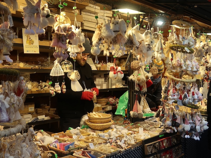 Puesto de mercadillo en Praga con adornos navideños y figuras de ángeles, rodeado de luces y decoración festiva.