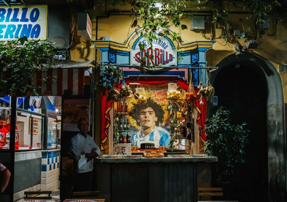 Fachada de la Pizzería Sorbillo en Nápoles con mural de Maradona y productos típicos de street food