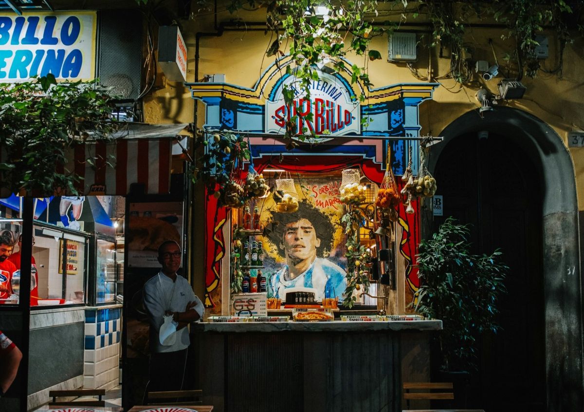 Fachada de la Pizzería Sorbillo en Nápoles con mural de Maradona y productos típicos de street food