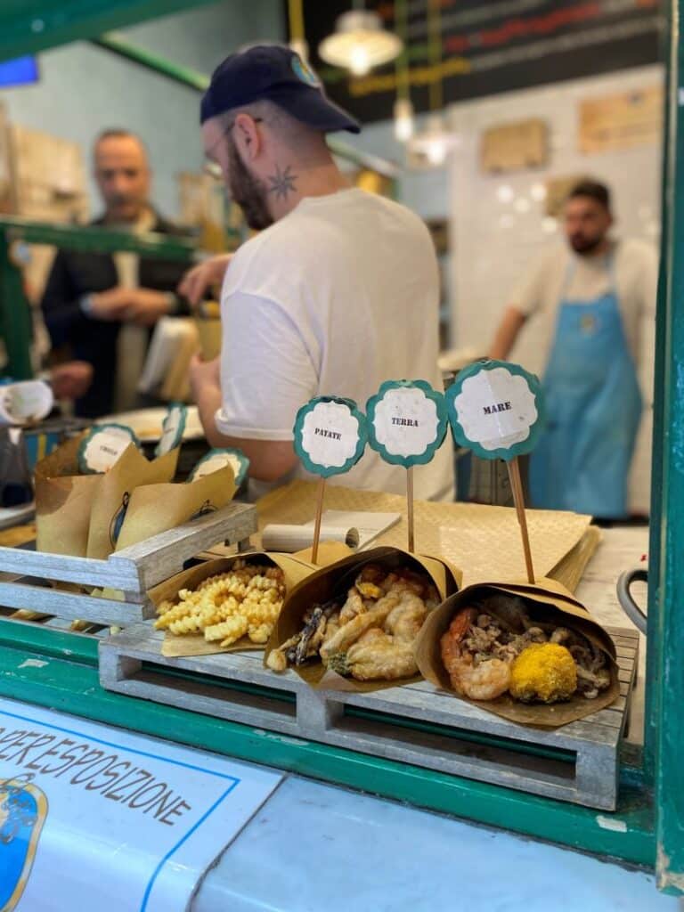 Para la foto del cuoppo, el objetivo es que Google te posicione tanto por el nombre del plato como por el concepto de "comida callejera", que tiene muchísimas búsquedas. Aquí tienes la mejor opción: Alt Text: Cuoppo di mare con fritura de pescado fresco en un cono de papel, el street food más típico que comer en Nápoles