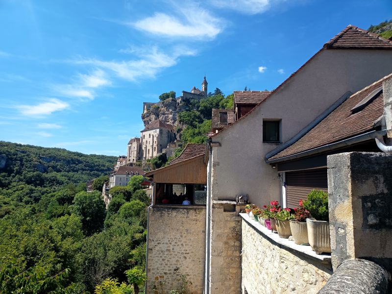 Vista lateral del pueblo medieval de Rocamadour, colgado en un acantilado sobre el valle en la región de Occitania, Francia, en un día soleado.