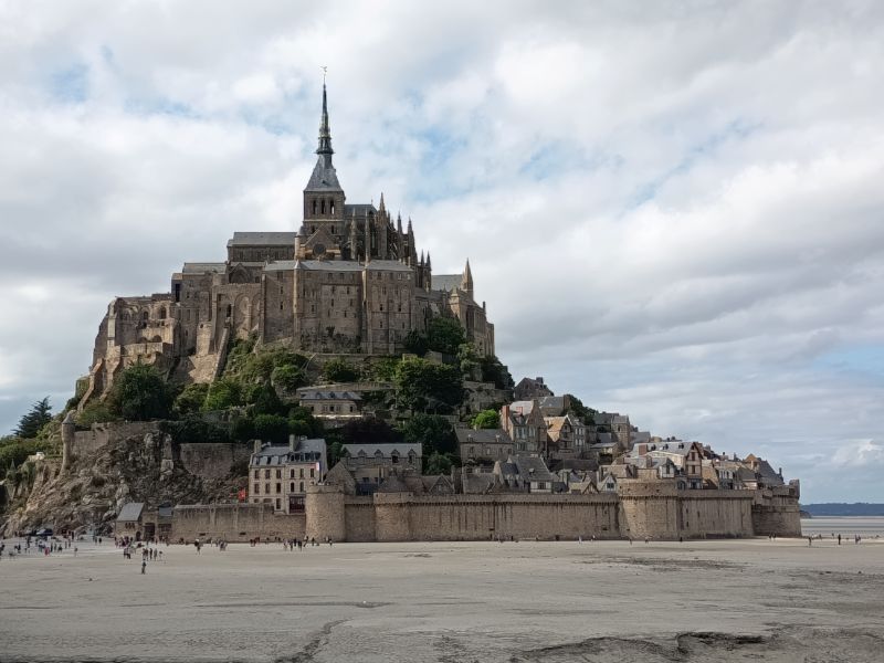 Vista panorámica de la abadía medieval del Mont Saint-Michel sobre la bahía en Normandía, Francia, en un día con nubes y claros.