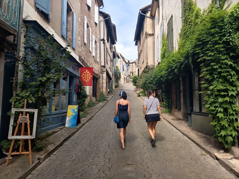 Mónica y Julieta caminando de espaldas por una calle estrecha y empedrada del pueblo medieval de Cordes-sur-Ciel en Francia