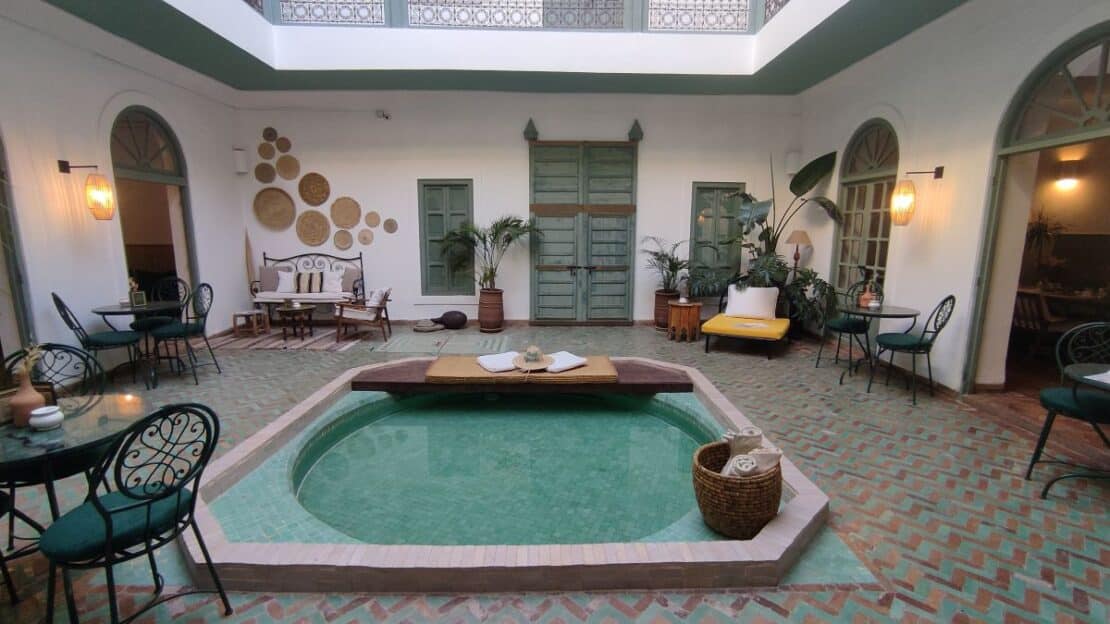 Patio interior de un riad tradicional en la Medina de Marrakech con azulejos zellige y plantas.