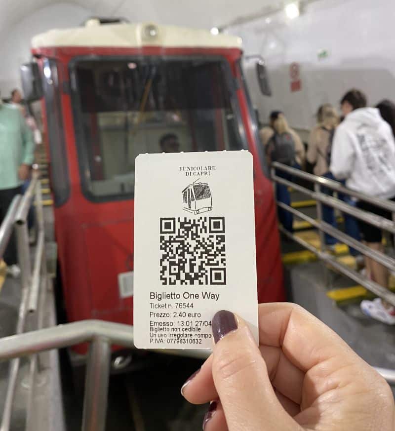 Billete del Funicular de Capri con código QR y precio de 2,40 euros frente al vagón rojo