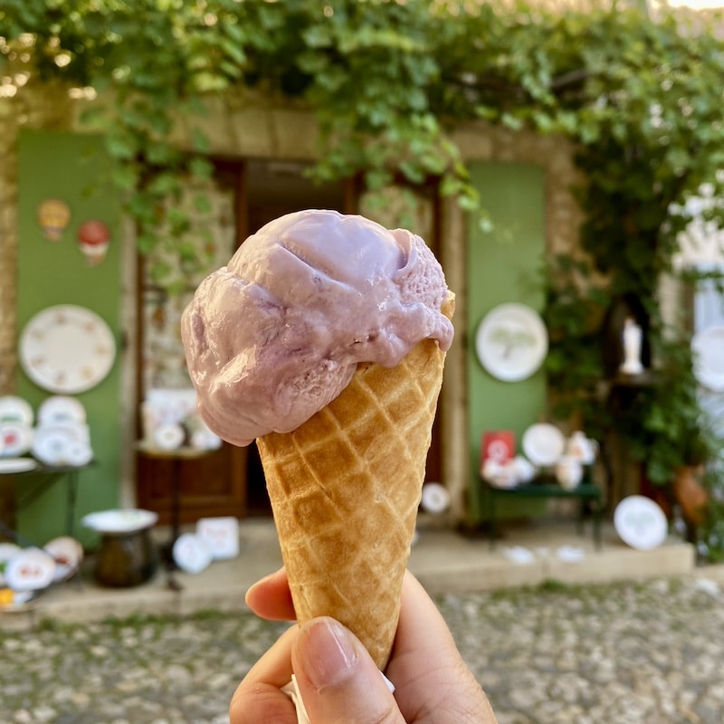 Helado artesano de color lila frente a una tienda de loza típica en Moustiers-Sainte-Marie.