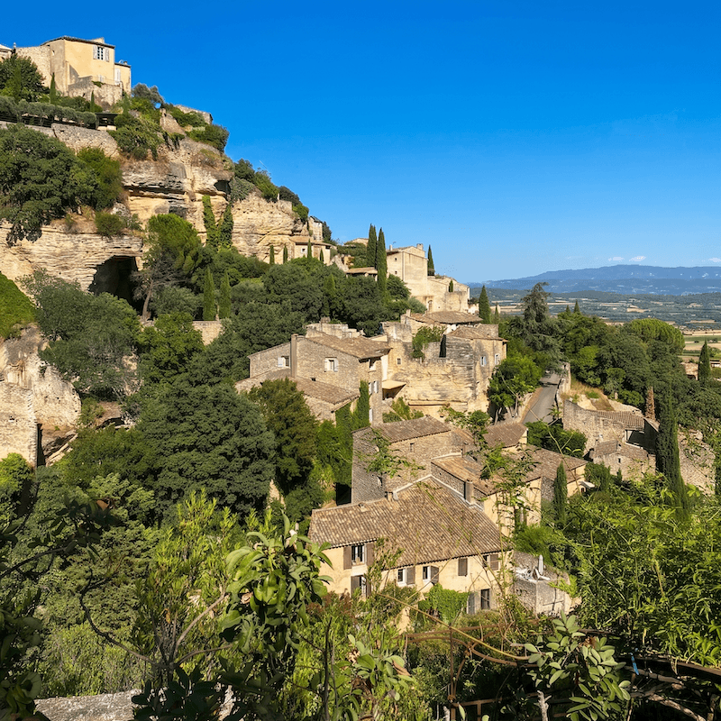 Vista panorámica del pueblo de Gordes construido sobre una colina con casas de piedra y vegetación verde.