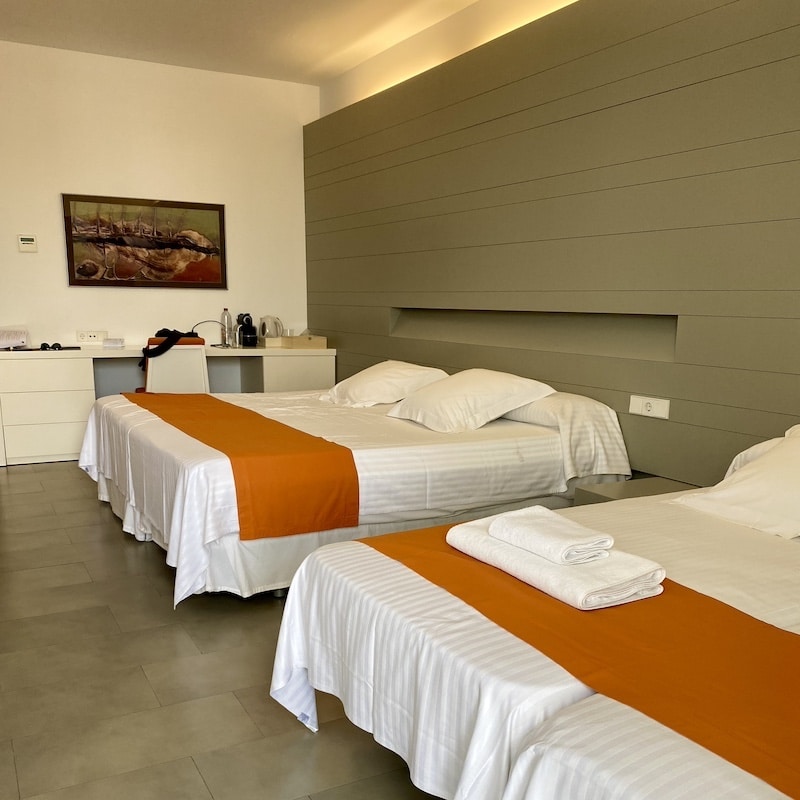 Detalle de una habitación de hotel en Las Negras, Cabo de Gata, con tres camas reales de sábanas blancas y decoración de madera.