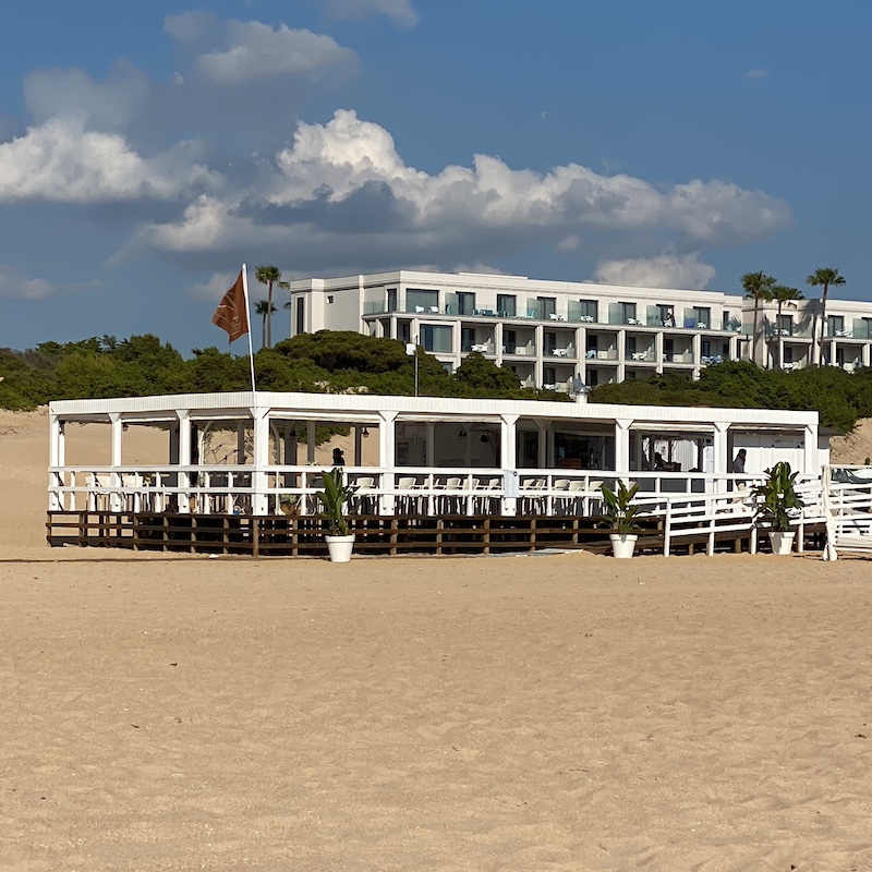 Fachada de un complejo hotelero blanco visto desde la arena fina y dunas de la Playa de la Barrosa en Chiclana.