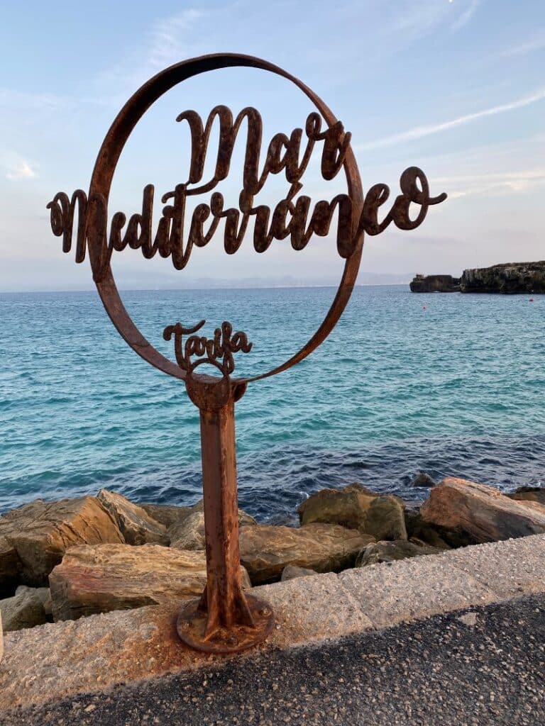 Escultura circular de hierro oxidado con las letras "Mar Mediterráneo" en el dique de la Isla de las Palomas en Tarifa.