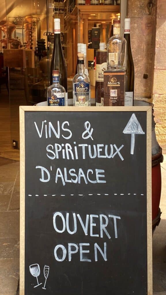 Pizarra informativa de una bodega con botellas de vino y licores artesanales para comer en Alsacia