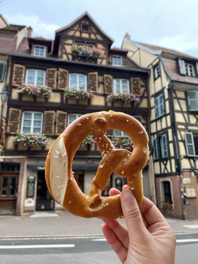 Bretzel salado tradicional con una casa alsaciana de entramado de madera de fondo