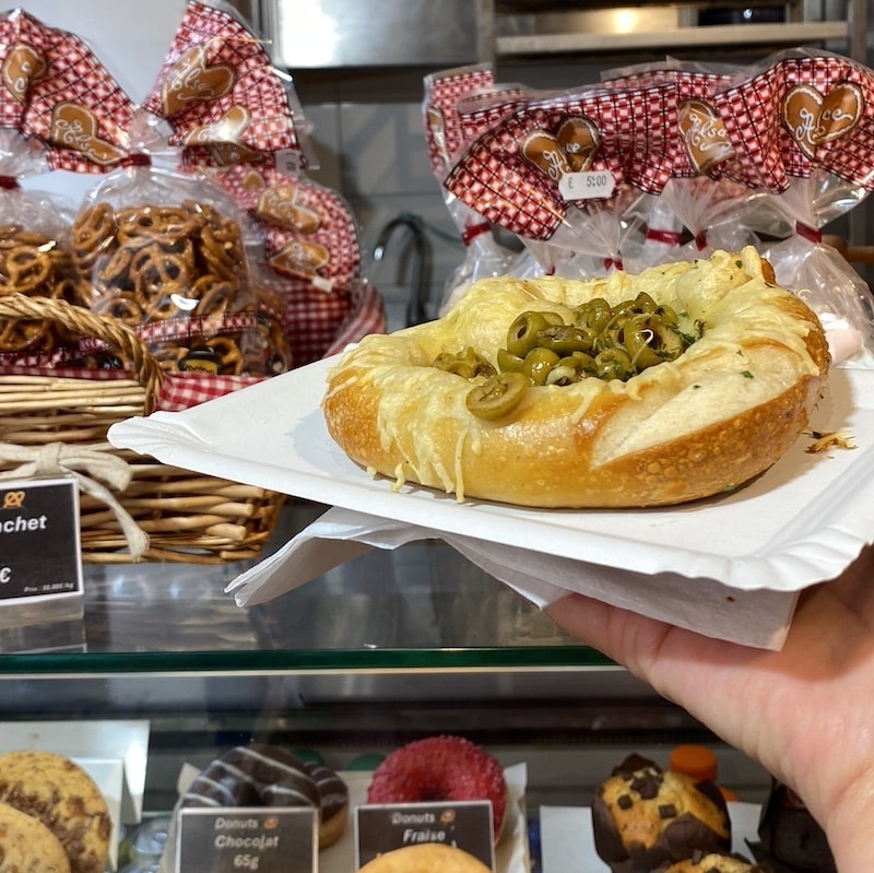 Mano sosteniendo un bretzel salado cubierto de queso derretido en una calle de Riquewihr