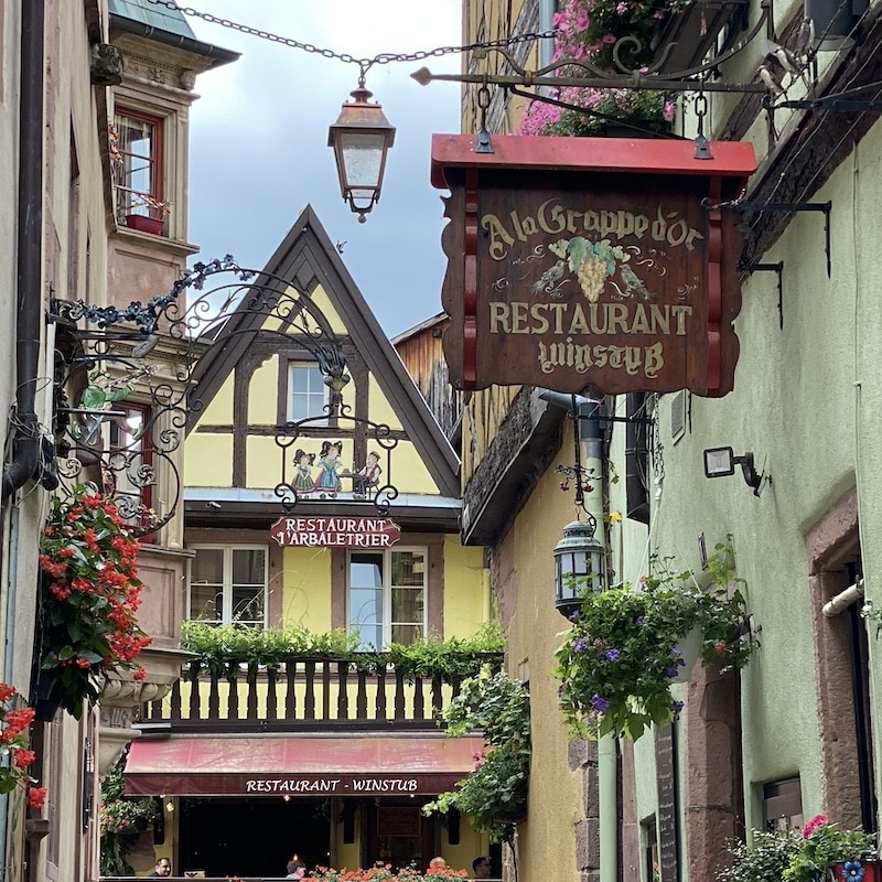 Fachadas tradicionales de entramado de madera de colores y carteles artesanos de hierro en Riquewihr