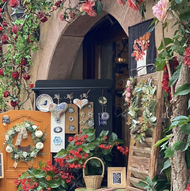 Fachada de tienda tradicional decorada con plantas y flores en el casco antiguo de Kaysersberg.